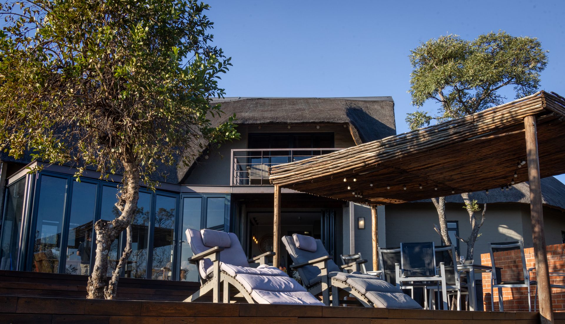 A safari lodge patio with sun loungers under a wood pergola